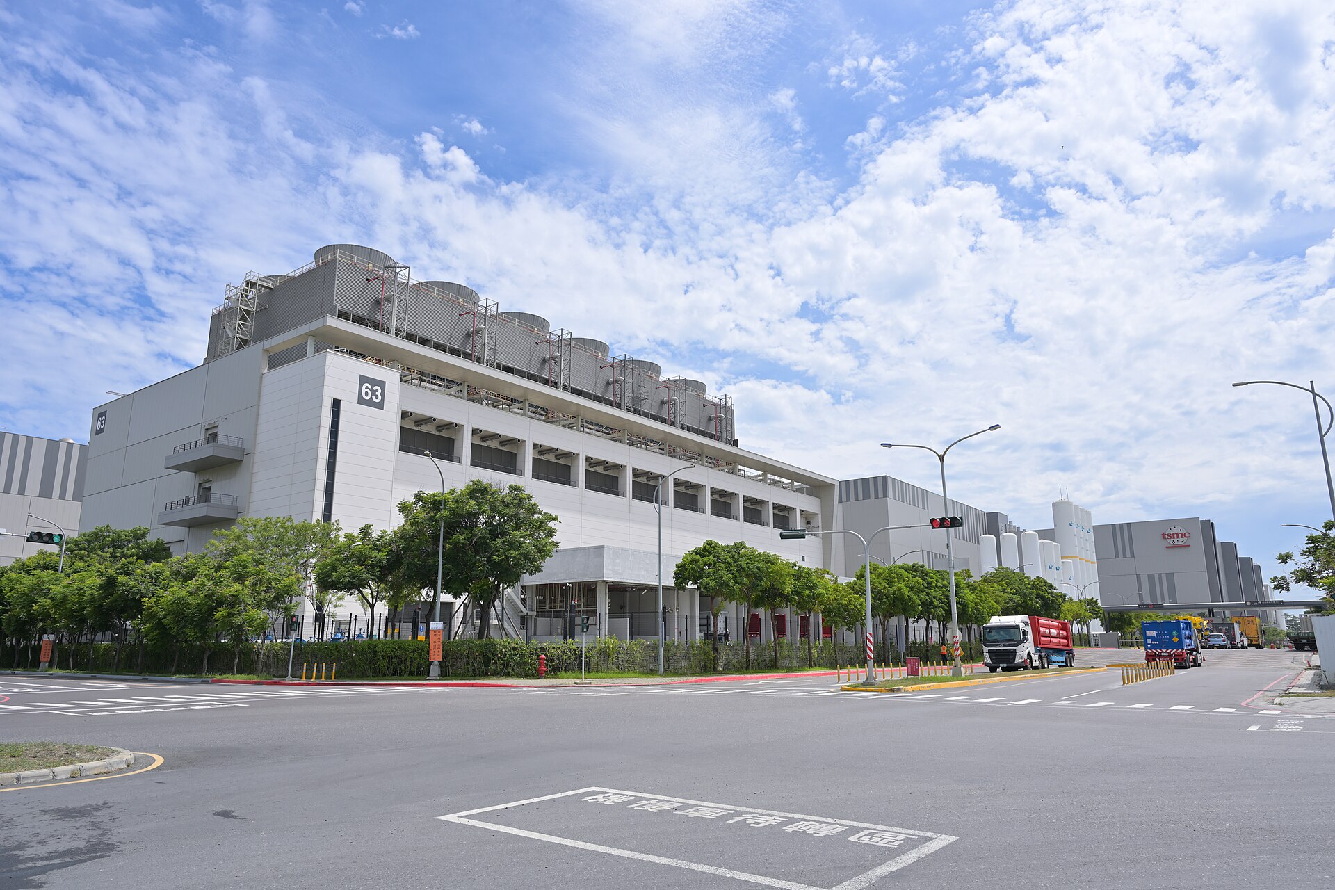Tarlaların yanında, çok büyük, beyaz ve gri bir fabrika binası: TSMC Fab 18