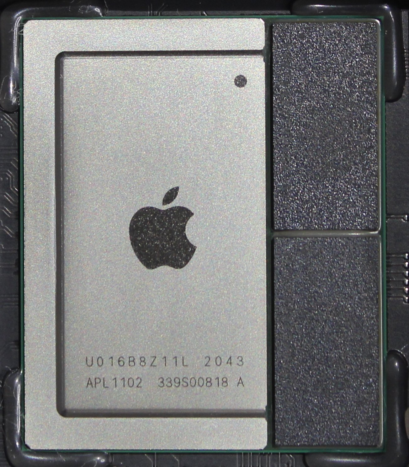 Bir Mac mini anakartı üzerinde Apple M1 yongası: solda üzerinde Apple logosu olan gümüş renkli kapak, sağda iki koyu renkli bellek yongası, hepsi aynı paketin üzerinde