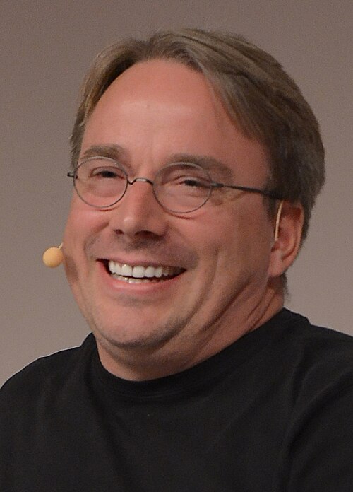 Gözlüklü, gülümseyen, siyah tişörtlü Linus Torvalds